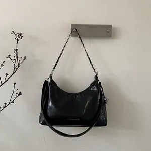 Détail du sac hobo en cuir verni noir avec chaîne argentée et texte imprimé blanc