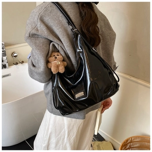 Detail of black glossy patent leather hobo bag with a cute plush bear charm and metal logo