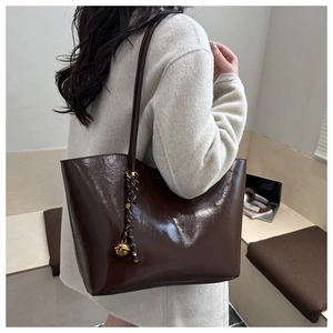 Close-up of brown oil wax leather tote bag featuring a gold bell charm and long shoulder strap