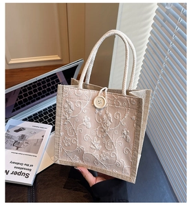 Close-up of beige linen handbag featuring delicate white floral embroidery and button closure