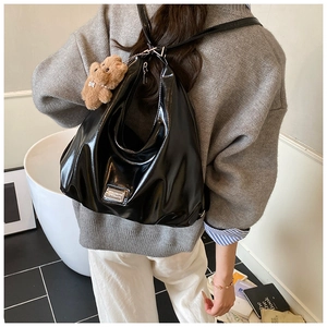Detail of high-gloss black patent leather tote bag with a brown plush bear keychain charm