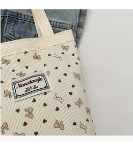 Detail of white corduroy tote bag showing strawberry and bow patterns with fabric patch