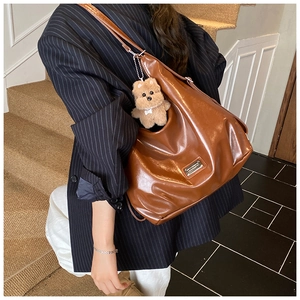 Detail of brown glossy tote bag with teddy bear pendant worn by a model in a suit