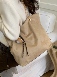 Large khaki corduroy tote bag with gold chain straps and cute animal charms on a sofa