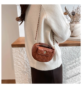 Detail of brown quilted crescent bag featuring a gold flower clasp and chain strap