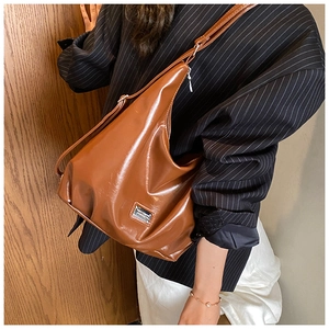 Close-up of caramel leather tote bag with metallic plate worn by model in stripe blazer