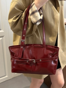 Retro burgundy patent leather shoulder bag with silver buckles worn with a trench coat