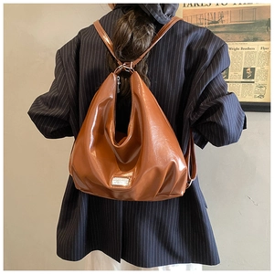 Detail view of the glossy dark brown leather backpack with silver metal logo plaque