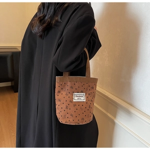 Close-up of brown corduroy tote bag with black bow and heart patterns and brand label