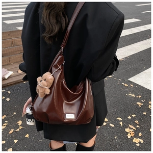 Detail of a large brown tote bag in oil wax leather finish with a cute teddy bear charm