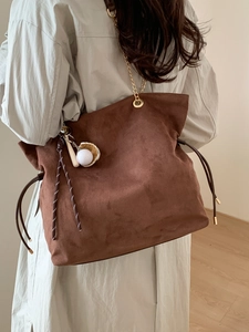 Brown suede tote bag with chain strap and drawstring detail on model in warm indoor setting