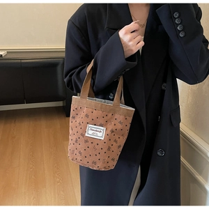 Detail of brown corduroy tote bag with black heart patterns and white logo label