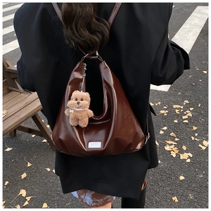 Detail of dark brown leather hobo bag with silver logo plate and plush bear charm