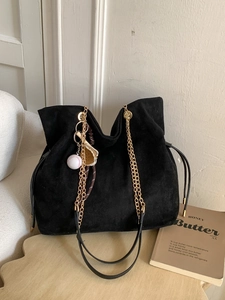 Black suede tote bag with golden chain handles and a baseball charm on a side table