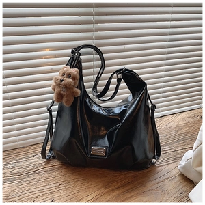 Detail of glossy black leather tote bag featuring a cute brown plush bear charm accessory
