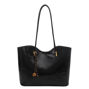 Minimalist black oil wax leather tote bag with slender straps and woven bell charm accessory