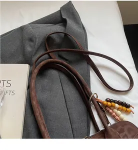 Close-up of brown suede shoulder bag with long strap and colorful wooden bead charm