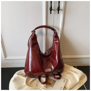 Detail of glossy deep red hobo bag with a rectangular silver metal plate and smooth finish