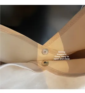 Macro view of strong magnetic clasp and canvas fabric texture on a beige bucket bag