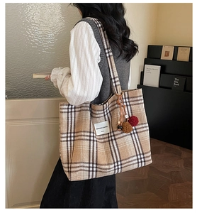Detail view of large canvas tote bag featuring brown plaid pattern and decorative pom-poms