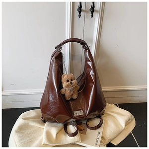 Detail view of coffee brown patent leather bag with metal logo and plush bear charm