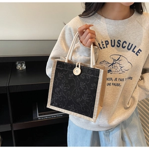 Detailed view of linen tote bag featuring black floral lace embroidery and button closure