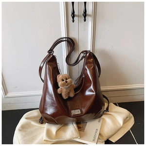 Detail shot of the large brown leather tote bag featuring a cute plush bear charm