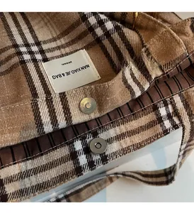Detail view of large tote bag with brown plaid pattern, magnetic snap, and striped lining