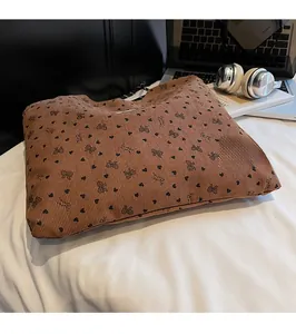 Detailed texture of brown corduroy tote bag with black heart and bow pattern on a bed