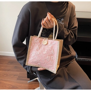 Close-up of pink floral embroidery on a linen handbag with white rope handles and button