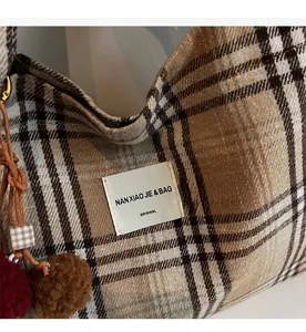 Detail of plaid canvas tote with a logo patch and decorative fur ball charms