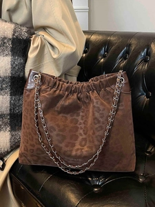 Retro brown leopard print suede tote bag with chain strap on a black leather sofa