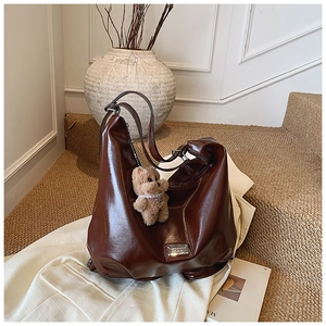 Detail of a dark brown glossy leather tote bag with a cute teddy bear charm