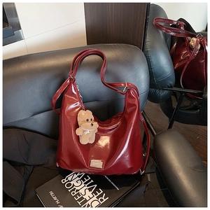 Detail of burgundy glossy faux leather hobo bag with a plush bear charm and silver logo