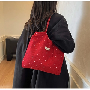 Detail of red floral tote bag with white daisy patterns and shoulder strap on a model