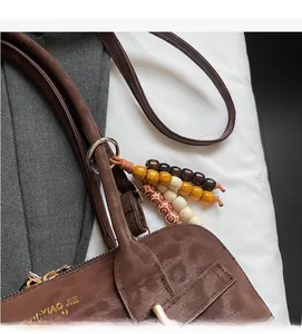 Detail of dark brown handbag showing beaded charm accessory and metallic texture