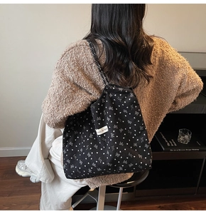 Detail of black corduroy tote bag featuring white bow patterns and branded woven label