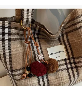 Detailed close-up of brown checkered tote bag with plush pom-pom and beaded charm