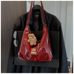 Close-up of burgundy PU leather hobo bag with metal logo and cute plush bear charm