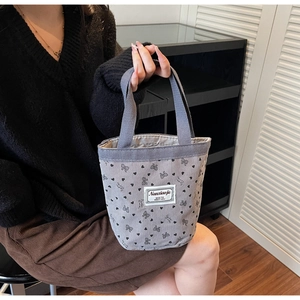 Detail showing grey corduroy tote bag with heart patterns and brand label in hand