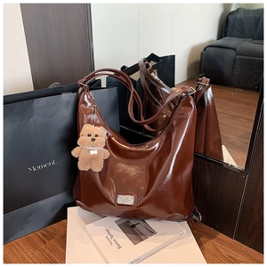 Detail view of large dark brown hobo bag in glossy wax leather with bear charm