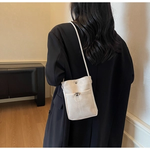 Vue arrière d'un mini sac à bandoulière beige minimaliste porté sur un blazer noir chic