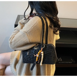 Close-up of black leopard texture handbag with gold lettering and colorful wood bead charm