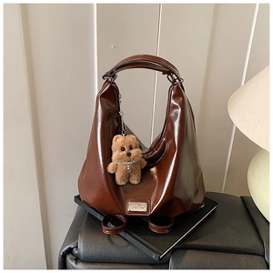 Detail of dark brown glossy hobo bag with silver plaque and plush bear charm