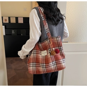 Detail of plaid tote bag with plush pom-poms shown on model in home setting