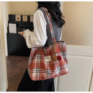 Close-up of red plaid wool tote bag with plush ball charms and brand label detail