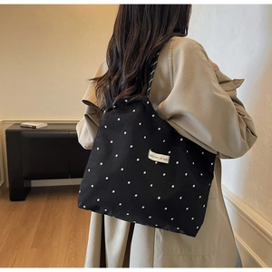 Detail view of large capacity black floral chiffon tote bag worn with a trench coat