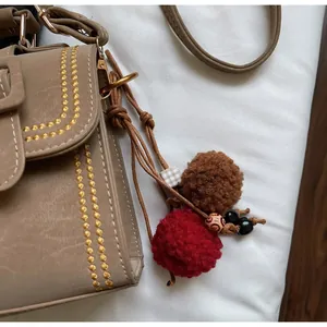 Detail der beige Tasche mit gelben Stickereien und buntem Pompon-Anhänger