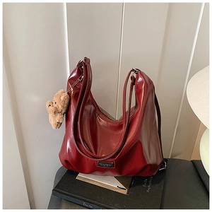 Detail of burgundy glossy tote bag with leather texture and cute brown plush bear charm