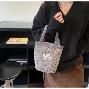 Detailed view of grey corduroy tote bag with bow prints held by a model in a cozy study